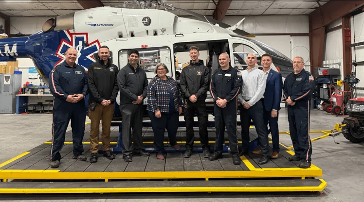 Aviation and medical team posing beside a helicopter inside a maintenance hangar.